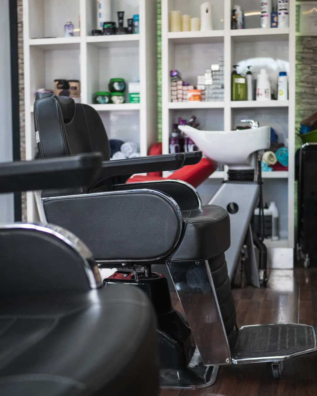 Zwei schwarze Coiffeurstühle im Salon, dahinter das Waschbecken und die Ablagen mit Pflegeprodukten