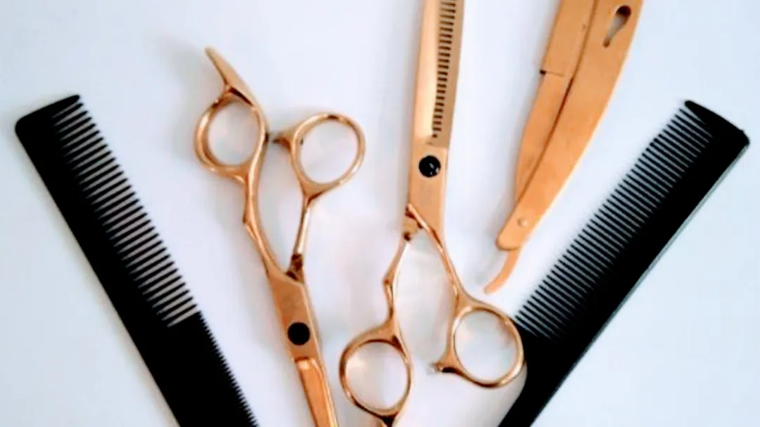 Goldene Haarschere, Effilierschere und Rasiermesser zwischen zwei schwarzen Kämmen
